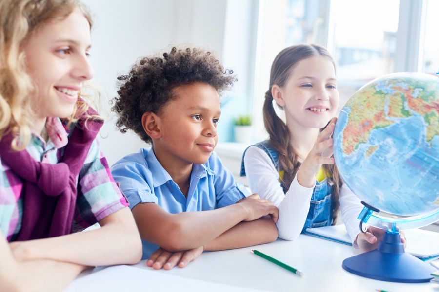 The Viridian Three children in a classroom examine a globe, engaged in learning about geography and world cultures.