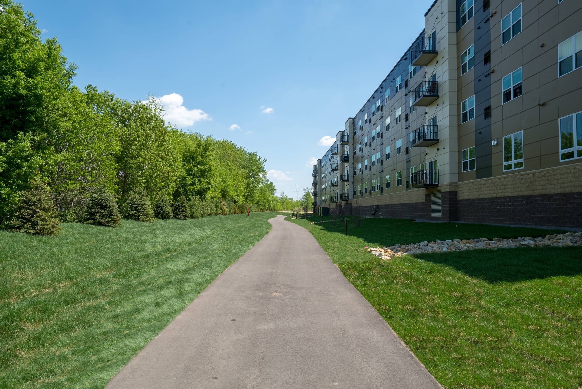 Viiridian Central Walking A pathway leading to a tall apartment building surrounded by greenery under a sunny sky.Trails
